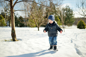 Fototapeta na wymiar Funny toddler boy having fun outdoors on chilly winter day. Child exploring nature.
