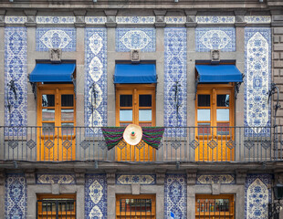 facade of colonial mexican house covered in blue talavera tiles, and a balcony with three doors,...