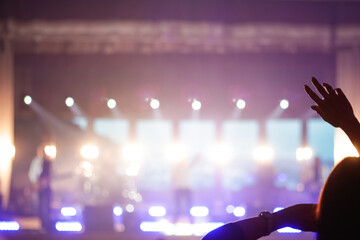 Defocus silhouette of one woman raise hand up in music concert with purple and white color spotlight on stage background. Out of focus