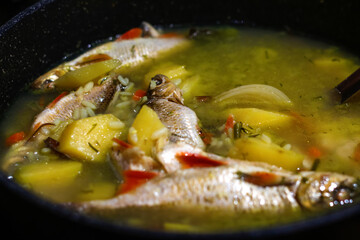 Defocus fish Soup Ukha. Perch fish in a clear broth with diced root vegetable served in white plate on wooden table. Selective focus. Fresh fish soup in pan. Out of focus