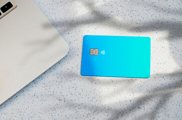 Plastic credit card with chip visible, on top of a table with soft lights and shadows. Blue card on white surface. Concept: finance, purchases, payments, loan, spending, investments and debts.