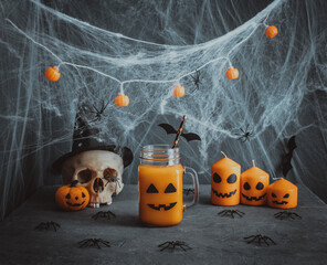 Halloween party decorations. Pumpkin juice with a jack-o-lantern face, cobwebs, candles and a skull...