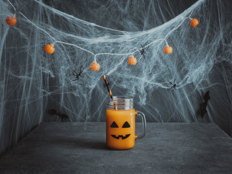 Halloween drink with jack o lantern face. Pumpkin cocktail in a glass jar on a dark blue background. Decorations for children's party. Copy space.