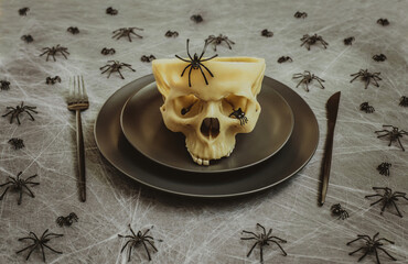 Fototapeta na wymiar Halloween table setting with black cutlery, skull and spiders in a web on a gray background. Creative festive serving.