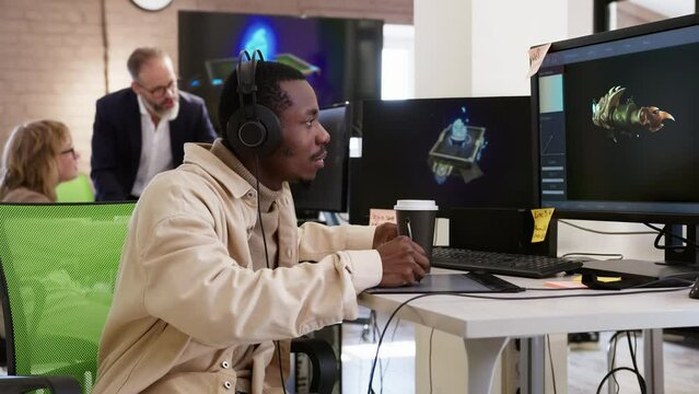African American male artist designer draws on a tablet a 3D models objects for a computer game in the office of a project development studio.