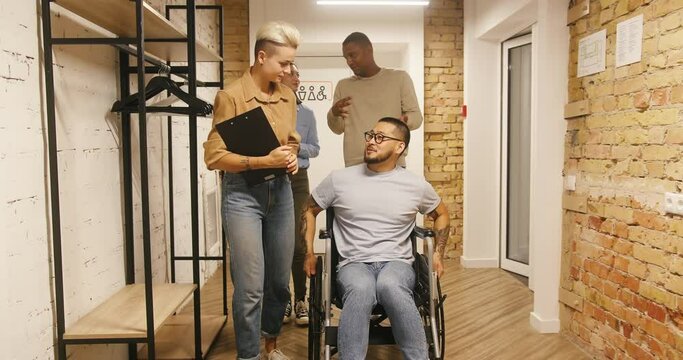Man in wheelchair listens to colleagues walking in office