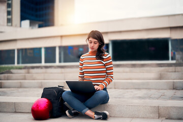 latin young woman sitting outdoors on the stairs with a laptop and a bag working