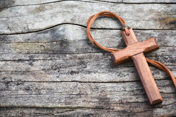 A wooden cross with a light brown leather strap rests on a wooden floor.