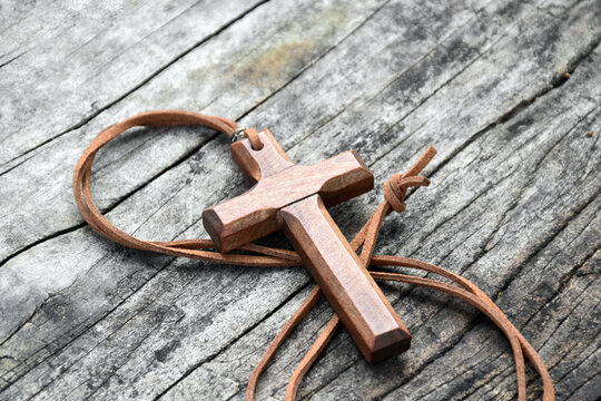 A wooden cross with a light brown leather strap rests on a wooden floor.