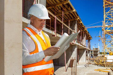 Builder at work. Man in work uniform near building. Builder carefully reads documentation. Man at...