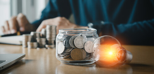 Businessman holding and putting lightbulb on coins stack on table for saving energy and saving money concept.