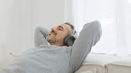 Happy relaxed Mature Adult man in headphones listening to the music and resting sitting on comfortable sofa in living room at home. Senior male sleeping on couch