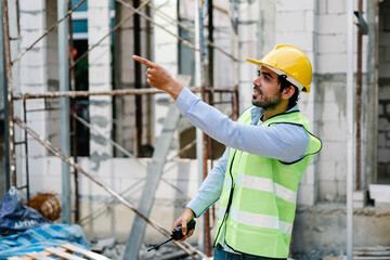 Engineering worker wearing a hardhat and vest, using a radio to provide instructions on the building construction site