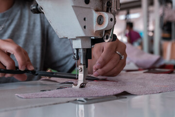 A seamstress cuts fabric while working at a sewing machine in the workshop. Women's hands