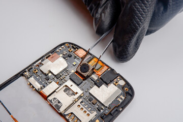 a smartphone repairman takes out a photo module from a smartphone with tweezers