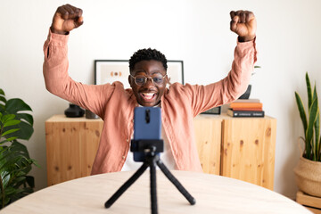 African American black male influencer live streaming with cellphone celebrating success with his...