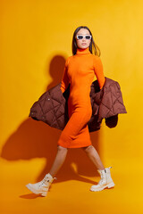 Fashion asian female model. Orange dress, down jacket, white boots, sunglasses. - 531363027