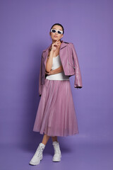 Fashion asian female model. Lilac leather jacket, lilac skirt, white boots, sunglasses.