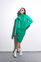 Fashion asian female model. Green total look. Green leather jacket, green dress, white boots, sunglasses.