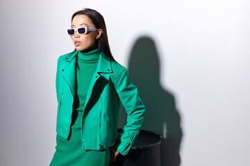 Fashion asian female model. Green total look. Green leather jacket, green dress, white boots, sunglasses.