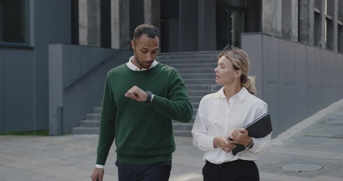 Businesspeople Discussing Business Plans with Each Other while Walking Outside at the Street. Multiracial Positive Man and Adult Woman Holding Laptop and Talking