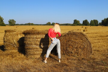 Naklejka na ściany i meble Beautiful young girl posing on a haystack. Sexy slim blonde relaxes in the autumn field at sunset.