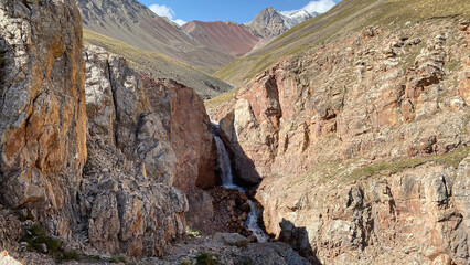 View from a height of a beautiful mountain waterfall. Green slopes, rocky mountains and hills of Kyrgyzstan. The amazing nature of the Pamirs.