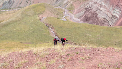 Fototapeta na wymiar Two climbers are climbing the mountain. View from a height of the colored rocky mountains, green slopes and hills of Kyrgyzstan. The amazing nature of the Pamirs.