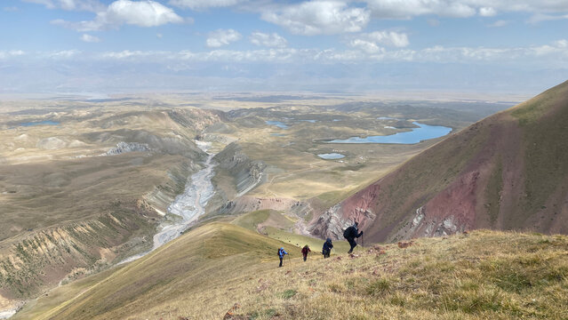 A group of tourists goes up the mountain. View from a height of the Alai Valley. Colored rocky mountains, lakes, rivers, green slopes and hills of Kyrgyzstan.