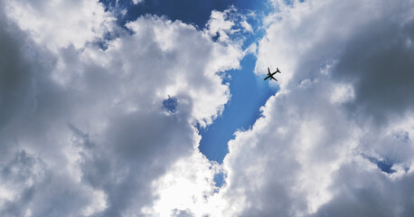 The passenger airplane is flying far away in the blue sky and clouds. Dramatic clouds with the sun shining through them. Aircraft in air. Horizontal stories. International passenger air transportation