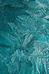 Abstract Christmas vertical background. Ice crystals on frozen window glass. Frost drawing. A pattern of leaves and stems of magical plant. Turquoise tinted winter wallpaper. Cold and crystal. Macro