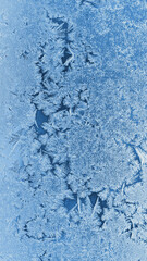 Abstract Christmas vertical background. Ice crystals on frozen window glass. Winter frost drawing. Blue mobile phone tinted wallpaper. Cold and crystal. Macro
