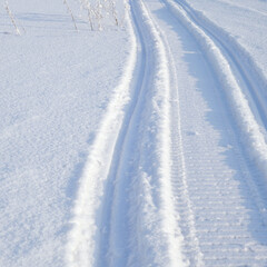 Track of traces from a snowmobile in drifts of white snow. Nature and outdoor on a winter sunny day. Square illustration with snowy field