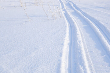 Track of traces from a snowmobile in drifts of white snow. Nature and outdoor on a winter sunny day. Background or wallpaper