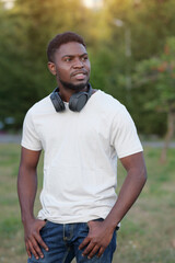 Young man wearing white t-shirt and jeans walks exploring nature in park. African American guy enjoys spending free time in city park at sunset