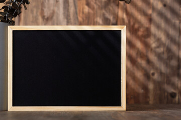 blank blackboard frame with kitchenware on wood table with sunlight