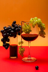 A glass of red wine and a bunch of grapes on a colored background