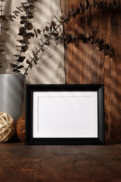 blank black photo frame with kitchenware on wood table with sunlight