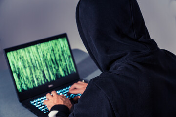 Hacker / Krimineller vor Laptop / Notebook mit schwarzem Kapuzenpullover