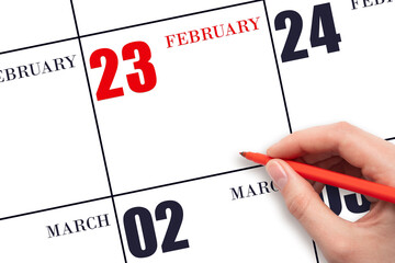 A hand holding a red pen and pointing on the calendar date February 23. Red calendar date, copy...