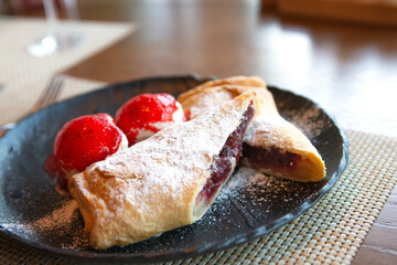 A popular dessert on the table is a cherry strudel cut into 2 halves with two balls of vanilla ice cream poured with strawberry jam. Strudel is powdered