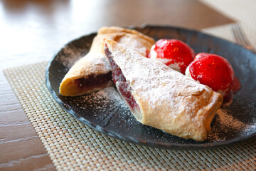 A popular dessert on the table is a cherry strudel cut into 2 halves with two balls of vanilla ice cream poured with strawberry jam. Strudel is powdered. Selective focus