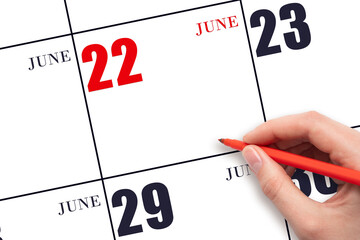 A hand holding a red pen and pointing on the calendar date June 22. Red calendar date, copy space,...