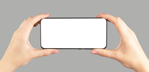 Hands holding phone mockup in horizontal position on grey background. Female watching video. Using digital technologies in modern life.