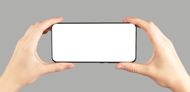 Hands holding phone mockup in horizontal position on grey background. Female watching video. Using digital technologies in modern life.