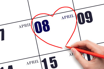 A woman's hand drawing a red heart shape on the calendar date of 8 April. Heart as a symbol of love.