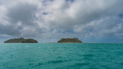 Obraz premium Two tropical islands are completely overgrown with green vegetation. A sandy beach is visible. The boat sails on the turquoise ocean. Blue sky with picturesque clouds. Seychelles