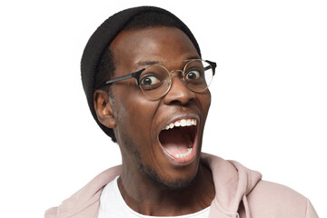 Emotional African man wearing trendy round eyeglasses looking at camera with eyes and mouth wide...