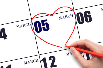 A woman's hand drawing a red heart shape on the calendar date of 5 March. Heart as a symbol of love.