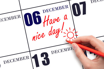 The hand writing the text Have a nice day and drawing the sun on the calendar date December 6